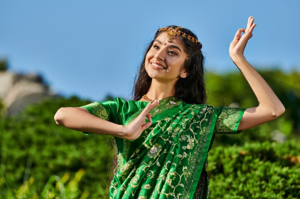pretty young indian woman in traditional sari dancing in blurred park with blue sky on background